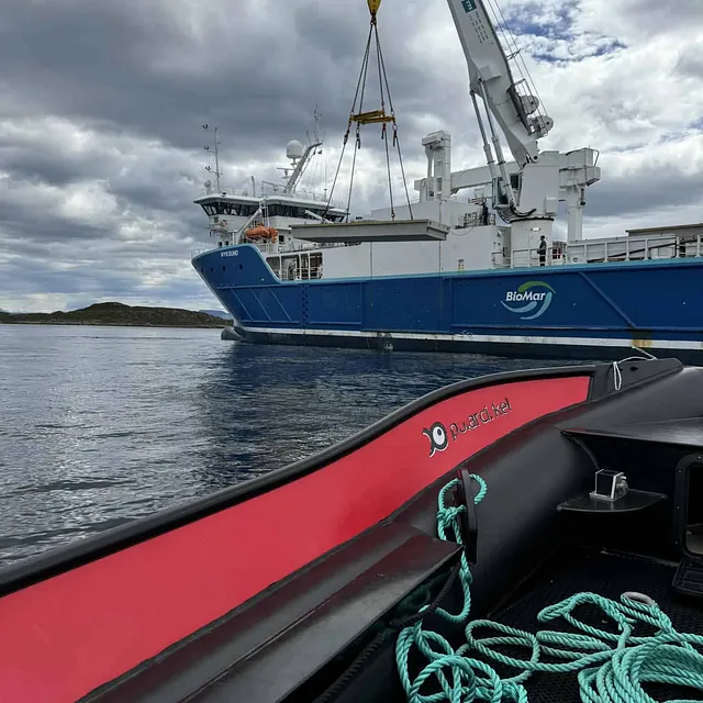 Kran på stor båt løfter utstyr fra vannet, sett fra en liten båt